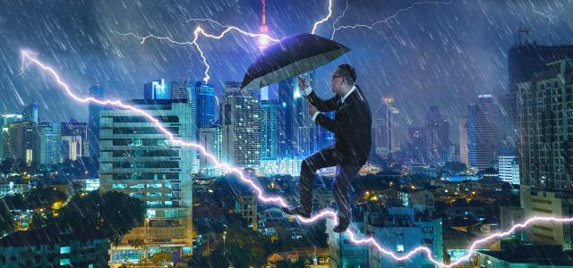 Young businessman with an umbrella bracing against a thunderstorm
